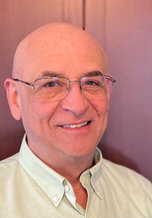 A man with glasses and bald head smiling.